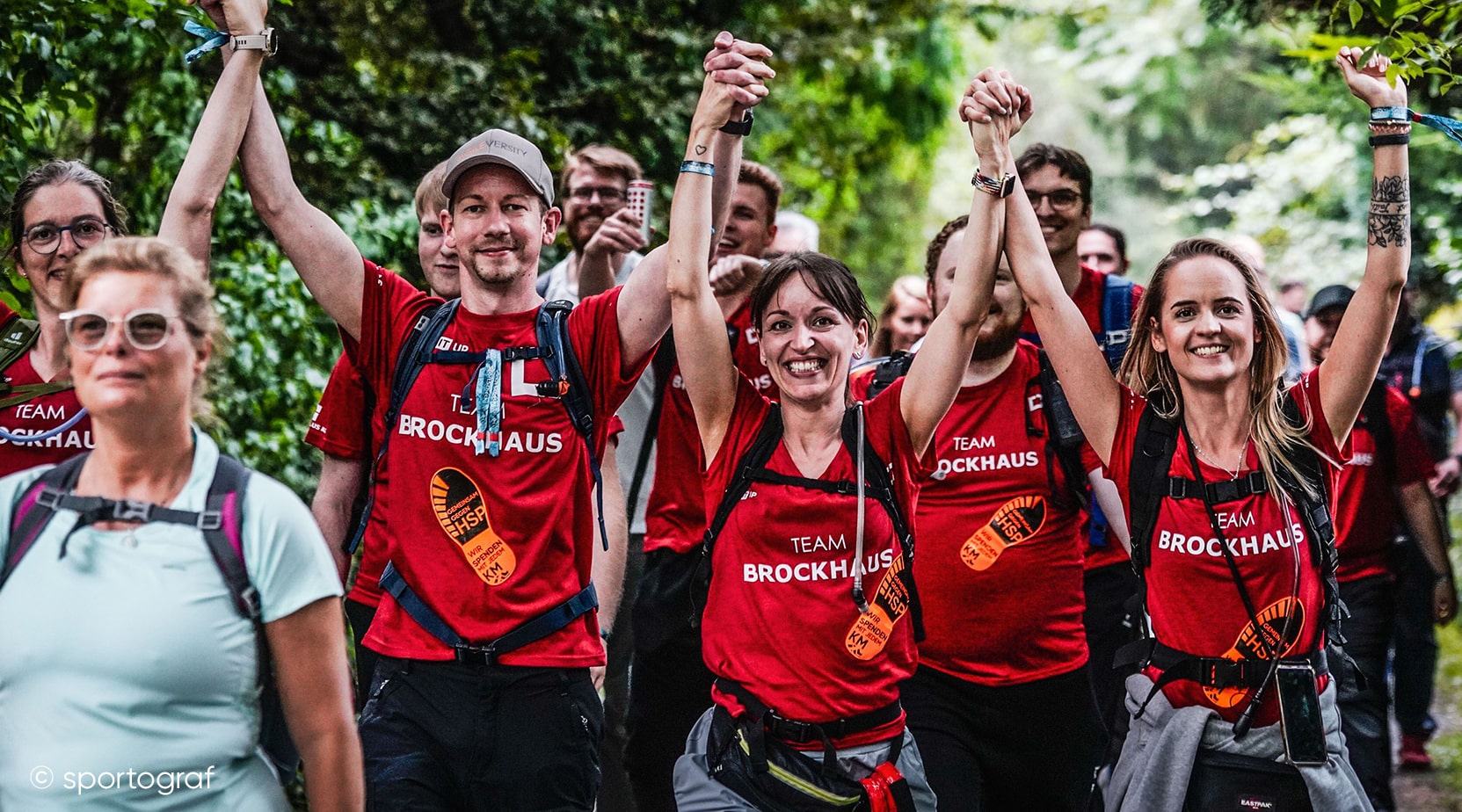 Mehrere Mitarbeitende in BROCKHAUS-Shirts halten sich beim Megamarsch Ruhrgebiet an den Händen und sammeln Spenden für die HSP-Forschung. Die Aktion dient der Unterstützung von Kollegin Christina Lempart's Tochter Mona.
