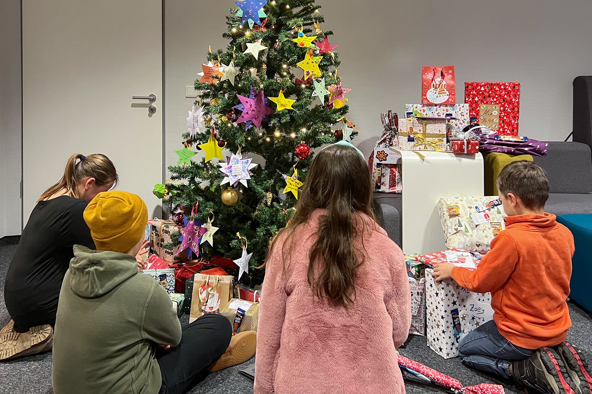 Die Kinder sitzen um den Baum und die Geschenke herum