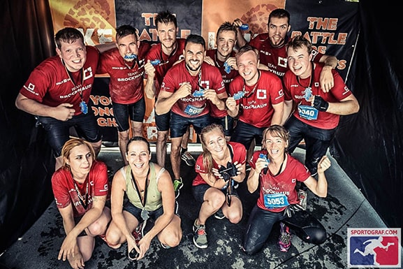 BROCKHAUS AG Team, stolz und schlammverschmiert, streckt ihre Medaillen nach dem LakeRun in die Kamera. Foto von einem unserer Teamevents.
